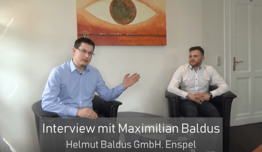 Aktuelles 77 Interview zwischen Maximilian Baldus und einem Gesprächspartner in einem modernen Büro, Helmut Baldus GmbH, Enspel. Im Hintergrund ein künstlerisches Wandbild.