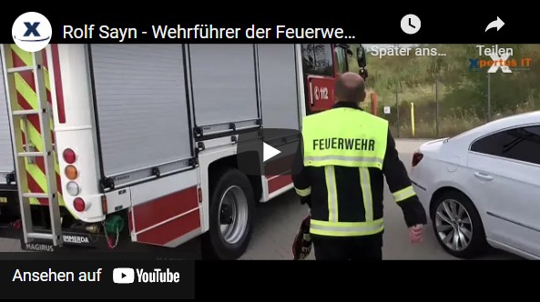 Aktuelles 50 Rolf Sayn, Wehrführer der Feuerwehr, geht neben einem Feuerwehrfahrzeug. Im Hintergrund ist ein weißes Auto zu sehen.