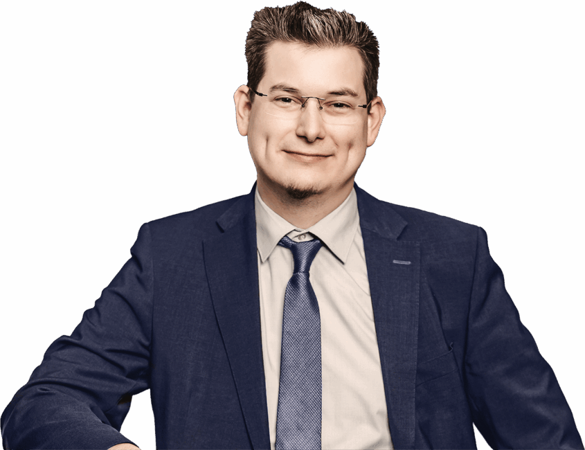 Mann mit Brille in einem blauen Anzug und Krawatte, lächelt in die Kamera.